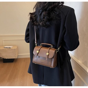 Detail of dark brown leather crossbody bag with gold buttons and fashion lettering