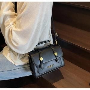Detail of black vintage messenger bag with matte leather and gold metal buckles