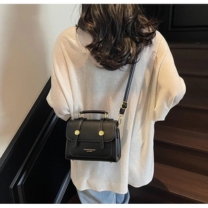 Fashionable black faux leather crossbody bag with gold studs shown on a model
