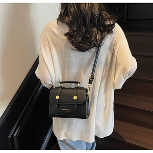 Detail of a chic black leather crossbody bag with gold rivets and adjustable strap