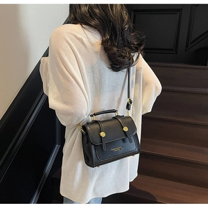 Rear view of a black leather handbag with golden buckles shown on a model