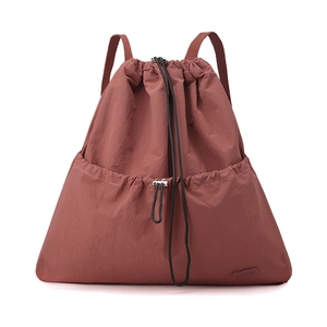 Detail view of brick red drawstring backpack with lightweight nylon texture and front pocket