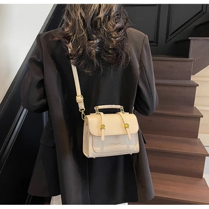 Detail of cream beige leather handbag with dual gold circular buckles and top handle
