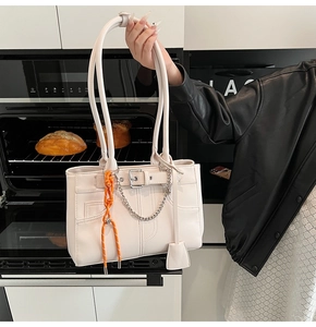 Detail of off-white leather tote bag with silver metal buckles and orange woven rope charm