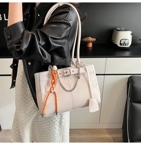Close-up of cream tote bag with silver chain, leather buckle and orange rope charm detail