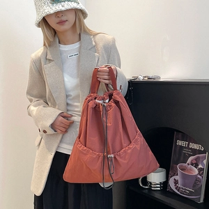 Detail of brick red drawstring tote bag with pleated texture held by a model