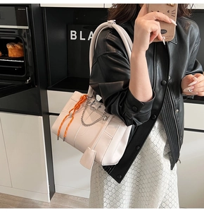 Detail of cream white tote bag with silver chain and orange woven charm on model