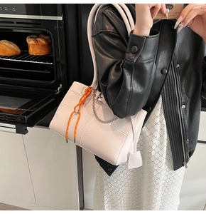 Detail of white leather tote bag with orange braided rope and silver chain accents