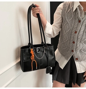 Detail of black faux leather tote with white stitching and silver chain ornament