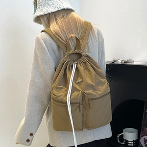 Detail shot of a khaki nylon drawstring backpack with two front zip pockets worn by a model
