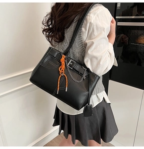 Detail of black leather tote bag with white stitching and orange braided rope charm