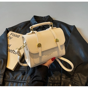 Detailed view of off-white leather crossbody bag with round gold buckles on black coat