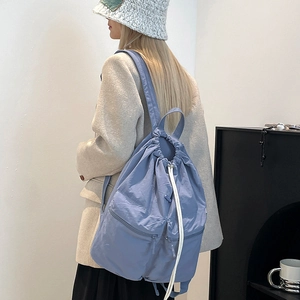 Close-up of light blue nylon drawstring backpack with zipper pockets on model