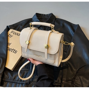 Detail of a beige leather crossbody bag with a gold circular buckle and top handle