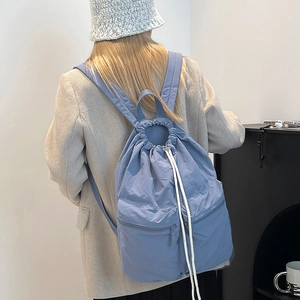 Model wearing a foggy blue nylon drawstring backpack with parallel front zipper pockets