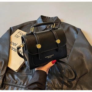 Close-up of black leather crossbody bag with dual gold buckles and embossed text logo