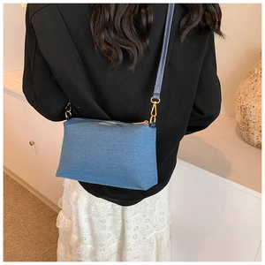 Détail d'un grand sac bandoulière en denim avec crochets dorés porté par un mannequin
