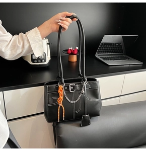 Detail of black leather tote with white stitching and decorative orange woven pendant