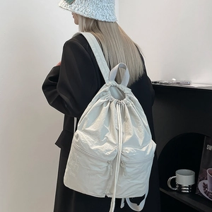 Detail view of cream nylon drawstring backpack with front zip pockets on model