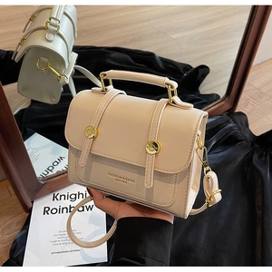 Close-up of beige leather messenger bag with gold studs and top handle detail
