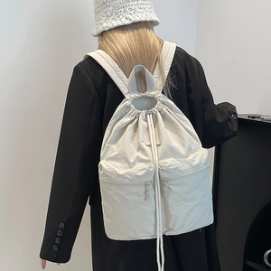 Detail of cream drawstring nylon backpack featuring dual front zipper pockets and straps