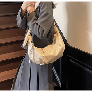 Detail of a beige crescent hobo bag with knotted shoulder strap and silver heart charm