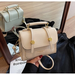 Close-up of cream leather handbag with gold metal buckles and embossed fashion logo