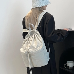 Detail of cream nylon backpack featuring drawstring closure and parallel zipper pockets
