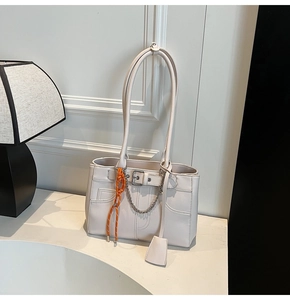 Detail of cream white tote bag featuring silver chain buckle and orange woven charm