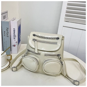 Detail van een crème witte mini rugzak van glanzend leer met metalen kettingen en ritsen