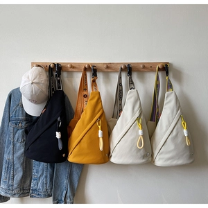 Three minimalist canvas crossbody bags in black yellow and cream hanging on a wooden wall