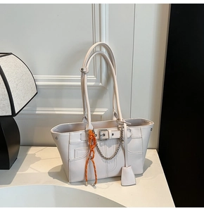 Detail of cream tote bag with silver chain, orange rope charm and smooth faux leather texture