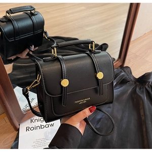 Detail of black leather crossbody bag with gold hardware and mirrored reflection
