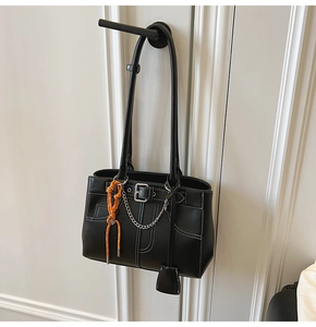Detail of black leather tote bag with white contrast stitching and orange cord on a door