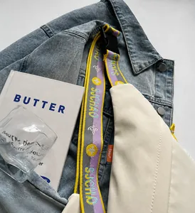 Detail of off-white canvas chest bag with colorful patterned strap on denim background