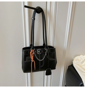 Detail of black tote bag with white contrast stitching and silver chain charm accessory