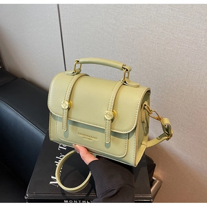 Close-up of bean green messenger bag with gold circular buckles and leather texture