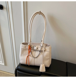 Detail of cream leather tote bag with stylish metal chain and orange braided rope accent