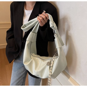 Detail of mint green hobo bag with knotted strap and woven pendant on a soft texture