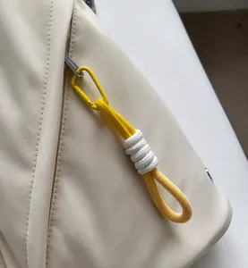 Detail of a smooth zipper with yellow carabiner and braided cord on a tan sling bag