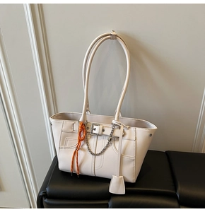 Detail of white leather tote bag with metal chains and orange braided charm accessory