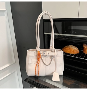 Detail of cream white leather tote bag with metal chain and orange climbing rope charm