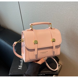 Pink leatherette crossbody bag with gold lock and handle, shown on a stylish display