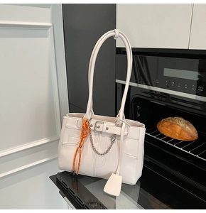 Detail of cream tote bag with silver chain heart charm and orange woven strap