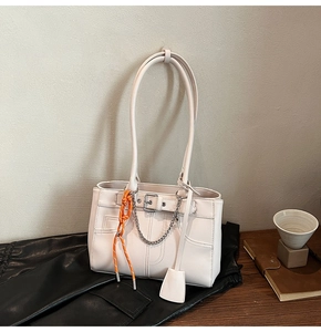 Close-up of cream shoulder bag with silver buckle, metal chain, and orange woven tassel