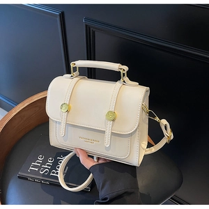 Detail of cream leather messenger bag with gold clasp on wooden stool