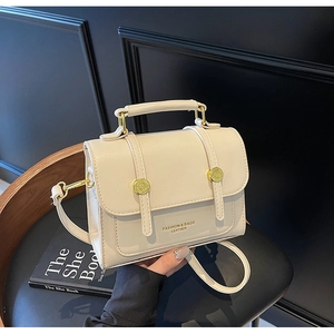 Close-up of cream leather crossbody bag with gold lettering and metallic studs