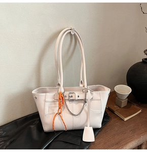 Detail of cream tote bag with orange braided pendant and silver chain on wooden table