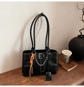 Detail of a black tote bag featuring white contrast stitching and silver chain accents