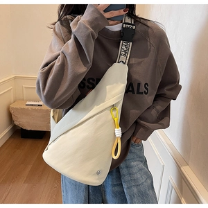 Detail of cream canvas sling bag featuring wide printed strap and yellow zipper charm